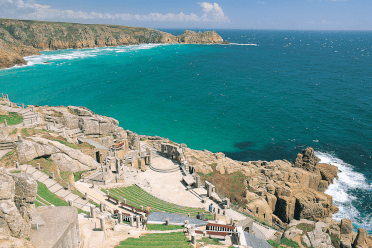 The Minack Theatre is cut into the coastline on the South West Coast Path, with open-air seating stepping down toward the sea and a distant headland looking impressive across the bay below.